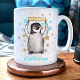 A personalised mug with an illustration of a baby penguin holding a sign which reads "Merry Christmas". The name Catherine is printed below the penguin.